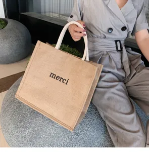 Close-up of a stylish large capacity jute tote bag with black merci text and white handles