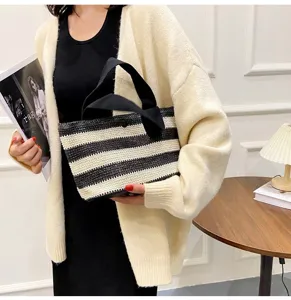 Gros plan d'un sac à main tissé à rayures noires et blanches tenu par un mannequin en cardigan.