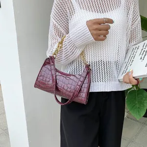 Detalle de bolso de hombro burdeos efecto cocodrilo con cadena dorada llevado por modelo