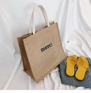 Detail of a casual jute tote bag with merci print and yellow summer sandals.
