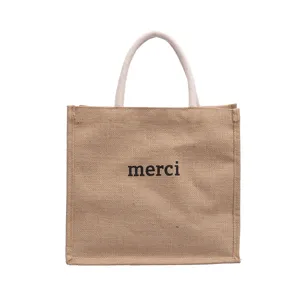 Front view of a natural jute tote bag with black 'merci' print and white rope handles