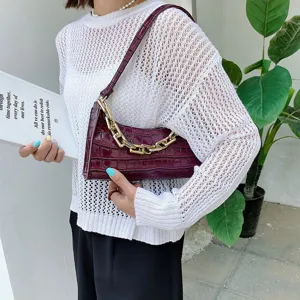 Detalle de un bolso de hombro burdeos con efecto de cocodrilo y una cadena dorada
