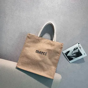 Detail of the natural jute fabric texture and 'merci' print on the stylish tote bag