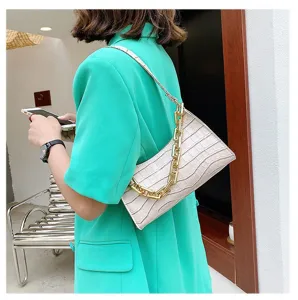 Detalle de bolso bajo el brazo crema con estampado de cocodrilo y cadena dorada