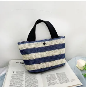 Détail d'un petit sac à main tissé à rayures bleues et blanches posé sur un magazine ouvert