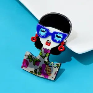 Macro detail of acrylic girl brooch with blue star glasses and floral dress pattern