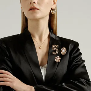 Detailed view of a three-piece vintage brooch set with a crystal number 5 on a black blazer.