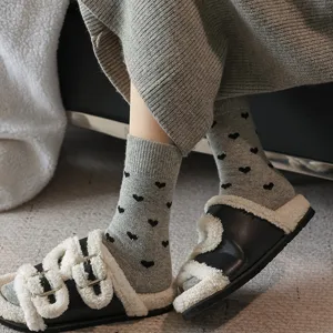 Cozy grey wool mid-calf socks with black heart patterns, paired with fluffy slippers for winter.