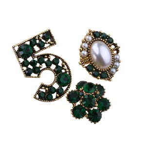 Detailed view of three vintage-style brooches featuring green crystals and a faux pearl