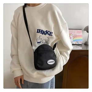 Vista detallada de un mini bolso bandolera de nailon negro con sudadera blanca