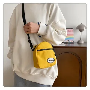 Detalle de un pequeño bolso bandolera de nailon amarillo sobre una sudadera blanca.