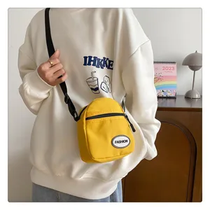 Bolso bandolera de nylon amarillo vibrante para móvil sobre una sudadera blanca.