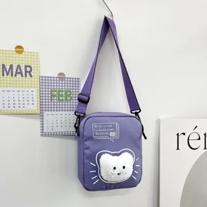 Vista detallada del bolso bandolera de nailon morado con decoración de cara de gato suave