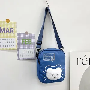 Detalle del bolso bandolera de nailon azul con una adorable cara de gato de peluche.