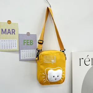 Primer plano de un bolso bandolera de nailon amarillo con un detalle de cara de gato.
