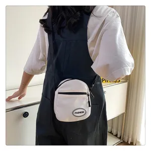 Detalle de un bolso bandolera de nailon blanco llevado con un peto negro