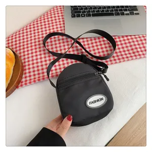 Primer plano del bolso bandolera de nailon negro con parche FASHION y cremallera.