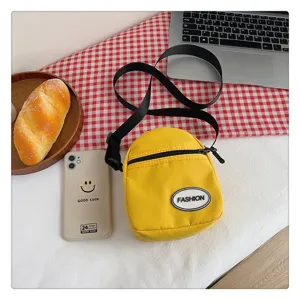 Bolso bandolera pequeño de nailon amarillo con parche FASHION en un entorno de escritorio
