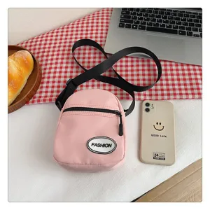 Detalle de bolso bandolera de nailon rosa con parche fashion y correa negra larga