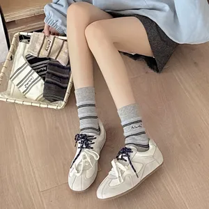 Close-up of grey striped socks with As You Wish embroidery on a female model wearing sneakers.