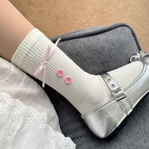 Close-up view of girls' white ribbed mid-calf socks featuring a pink bow and button detail