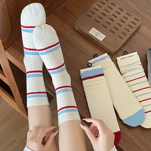 Détail de chaussettes mi-mollet en coton avec rayures rouges et bleues et bord volanté.
