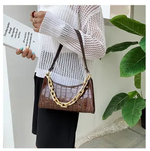 Detalle de bolso de hombro marrón con textura de cocodrilo y elegante cadena dorada chic