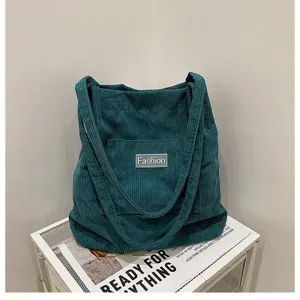 Detailansicht der petrolfarbenen Cordtasche mit Fashion-Label auf weißem Ständer