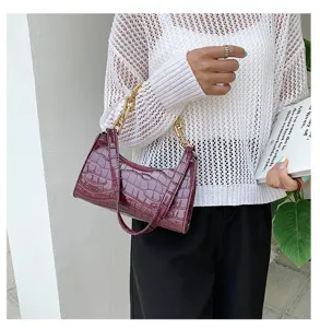 Detalle de cerca de un bolso burdeos con estampado de cocodrilo y cadena dorada gruesa.