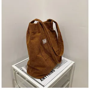 Detailansicht einer stilvollen braunen Cord-Tragetasche auf einem weißen Gitterregal.