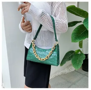 Detalle de bolso baguette verde con textura de cocodrilo y una cadena dorada gruesa