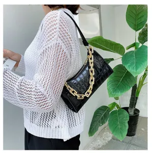 Vista detallada de un bolso de hombro negro con patrón de cocodrilo y cadena dorada en modelo.