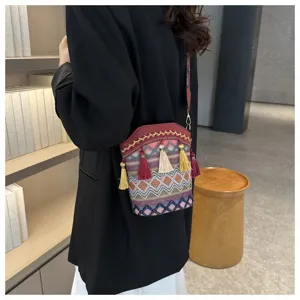 Gewebte Eimertasche im Ethno-Stil mit bunten Quasten auf einer schwarzen Blazerjacke