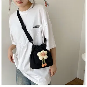 Detailansicht einer süßen schwarzen Canvas-Umhängetasche mit Plüschblume am Modell.