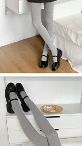Detailopname van grijze geribbelde panty met zwarte Mary Jane schoenen op witte plank.