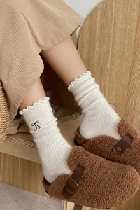 Chaussettes d'hiver blanches douillettes avec volants et broderie de nœud noir.