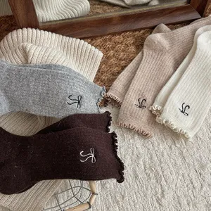 Gros plan de chaussettes en laine douillettes avec de fins volants et des nœuds brodés.