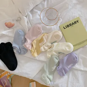Een verzameling pastelkleurige lage enkelsokken met hello-borduurwerk op een wit laken