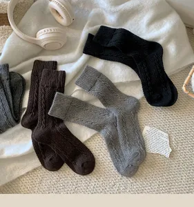 Close-up view of cozy cable-knit wool socks in black, brown, and grey, styled flat lay.