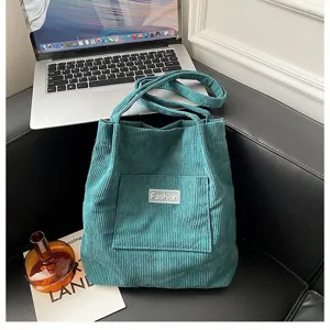 Modische petrolfarbene Cord-Einkaufstasche mit Vordertasche auf schwarzem Ledersofa