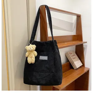 Elegante schwarze Cord-Umhängetasche mit Teddybären-Anhänger an einem Holzständer.