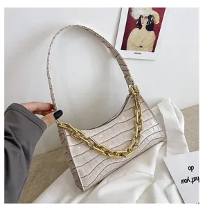 Detalle de bolso de hombro con textura de cocodrilo crema y una gruesa cadena dorada de moda.