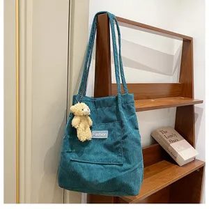 Nahaufnahme einer blauen Cord-Tasche mit süßem Bären-Anhänger und modischem Etikett