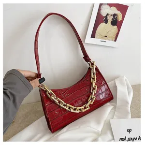 Primer plano de bolso baguette rojo oscuro con patrón de cocodrilo y cadena dorada gruesa