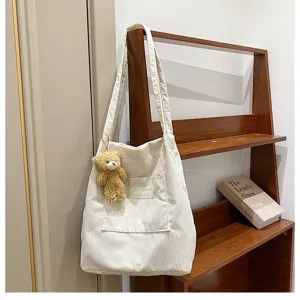 Detail einer weißen Cord-Einkaufstasche mit süßem Teddybär-Anhänger auf Holzregal