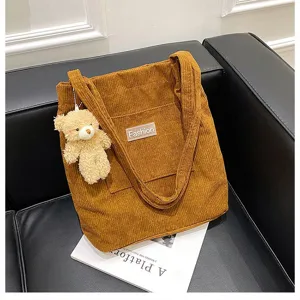 Detailaufnahme einer braunen Cord-Tragetasche mit Teddybär-Anhänger und Fashion-Label