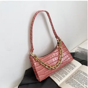 Vista detallada del bolso rosa con patrón de cocodrilo y cadena de oro decorativa.