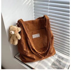 Detail einer braunen Cord-Tragetasche mit süßem Teddybär-Anhänger und Fashion-Label.