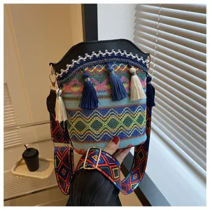 Nahaufnahme einer gewebten Eimer-Tasche im Ethno-Stil mit Quasten und buntem Gurt