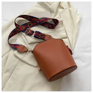 Detailansicht einer Vintage-Beuteltasche in Braun mit buntem Ethno-Gurt auf weißem Stoff
